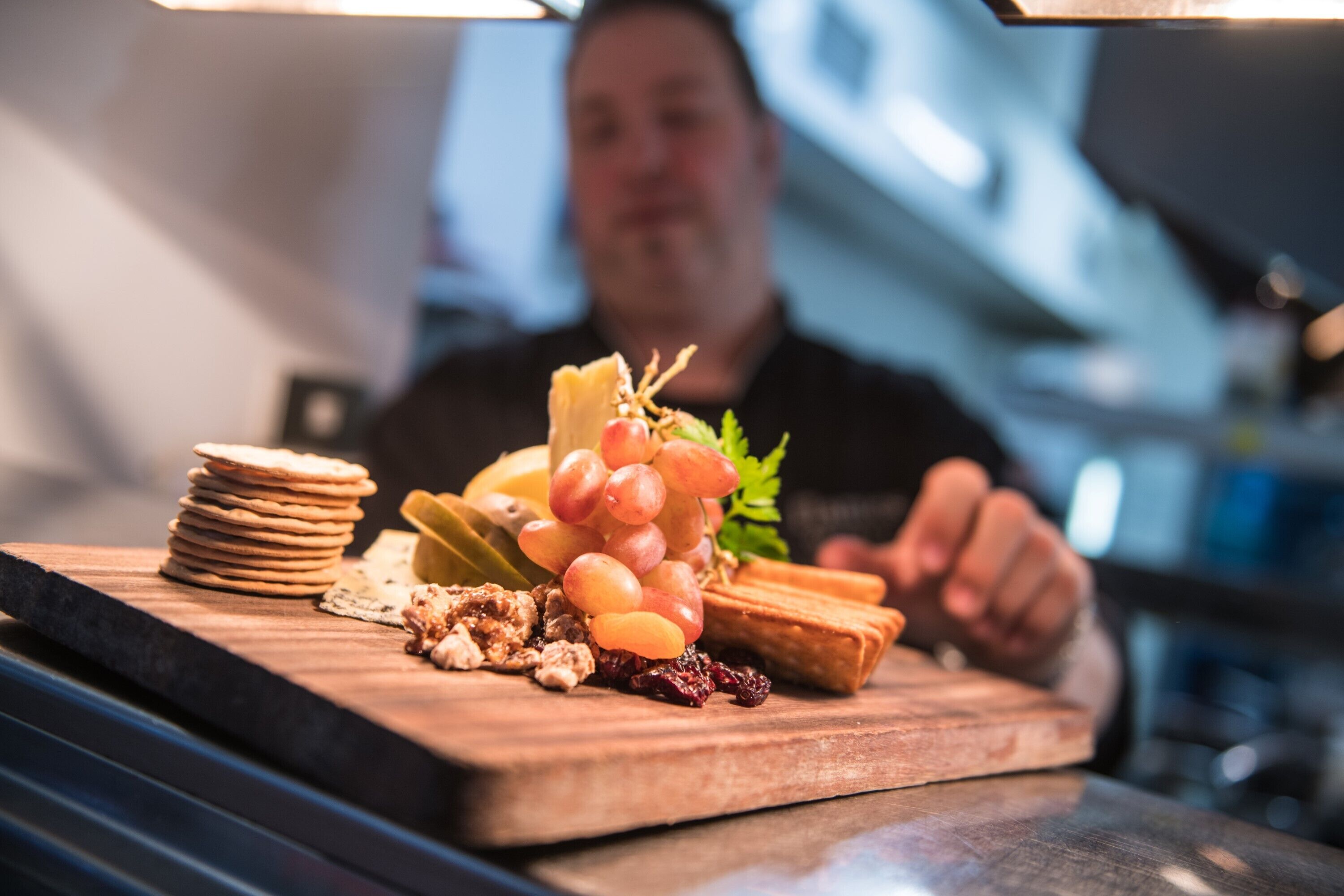 A wooden board with a variety of food items including grapes, cheese, and crackers.