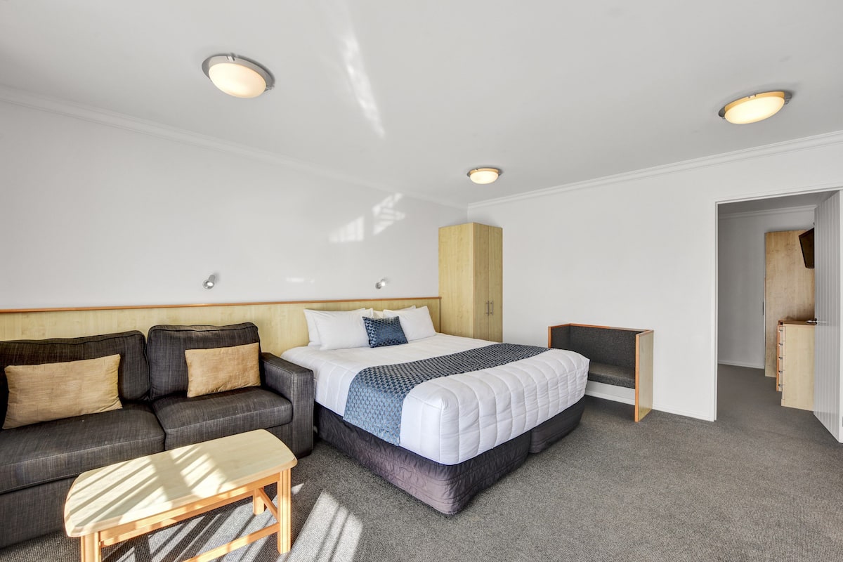 A modern hotel room with a bed, sofa, and a small table.