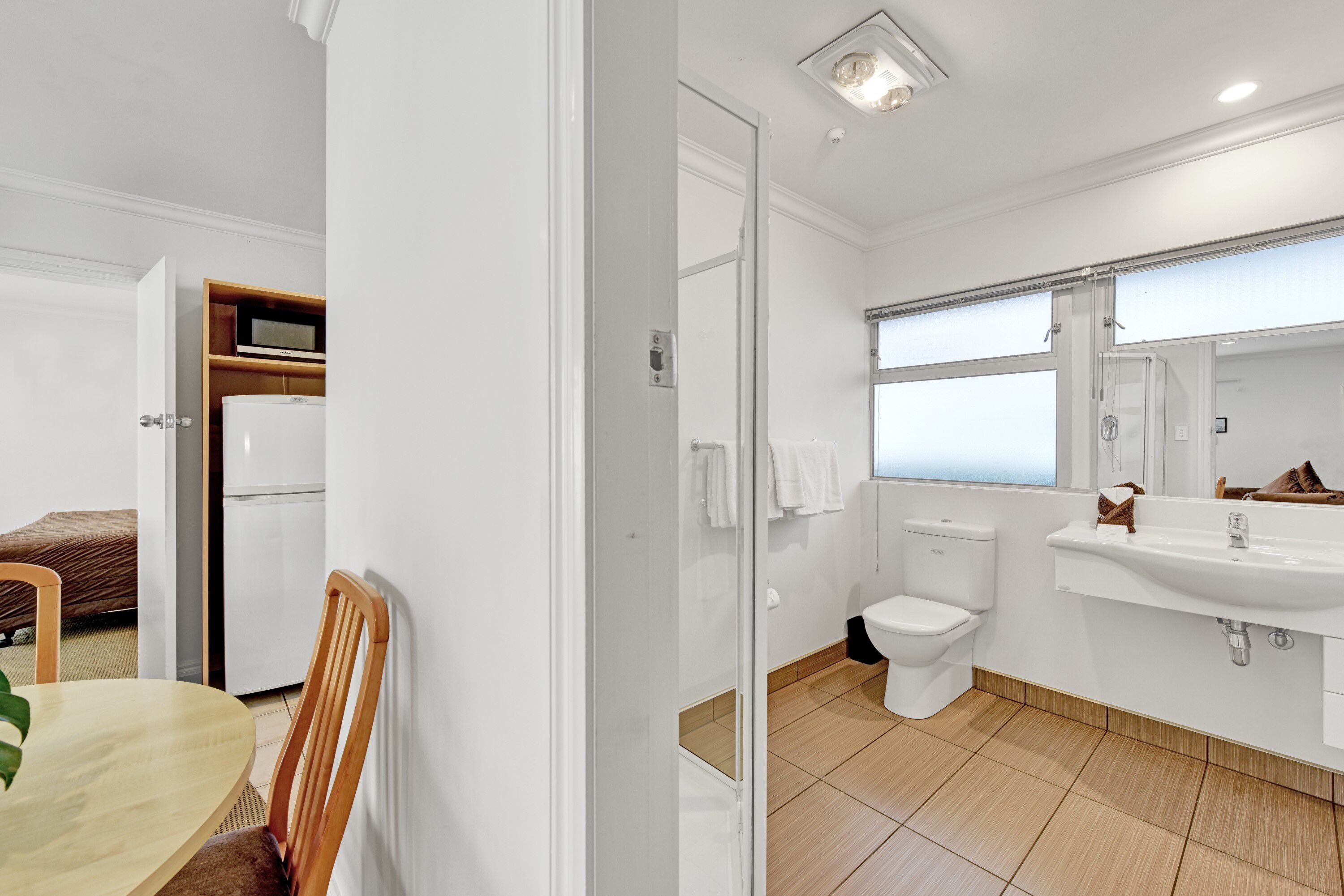 A modern bathroom with a toilet, sink, and mirror. There is a wooden chair and a table with a plant.