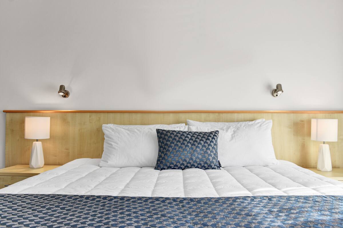 A neatly made bed with white bedding and a blue patterned pillow, flanked by two bedside lamps on wooden nightstands.