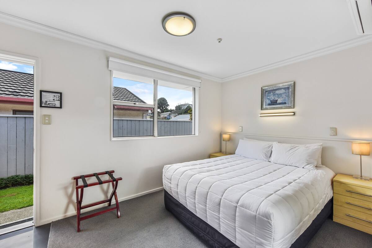 A bedroom with a bed, bedside tables, a window, and a door.