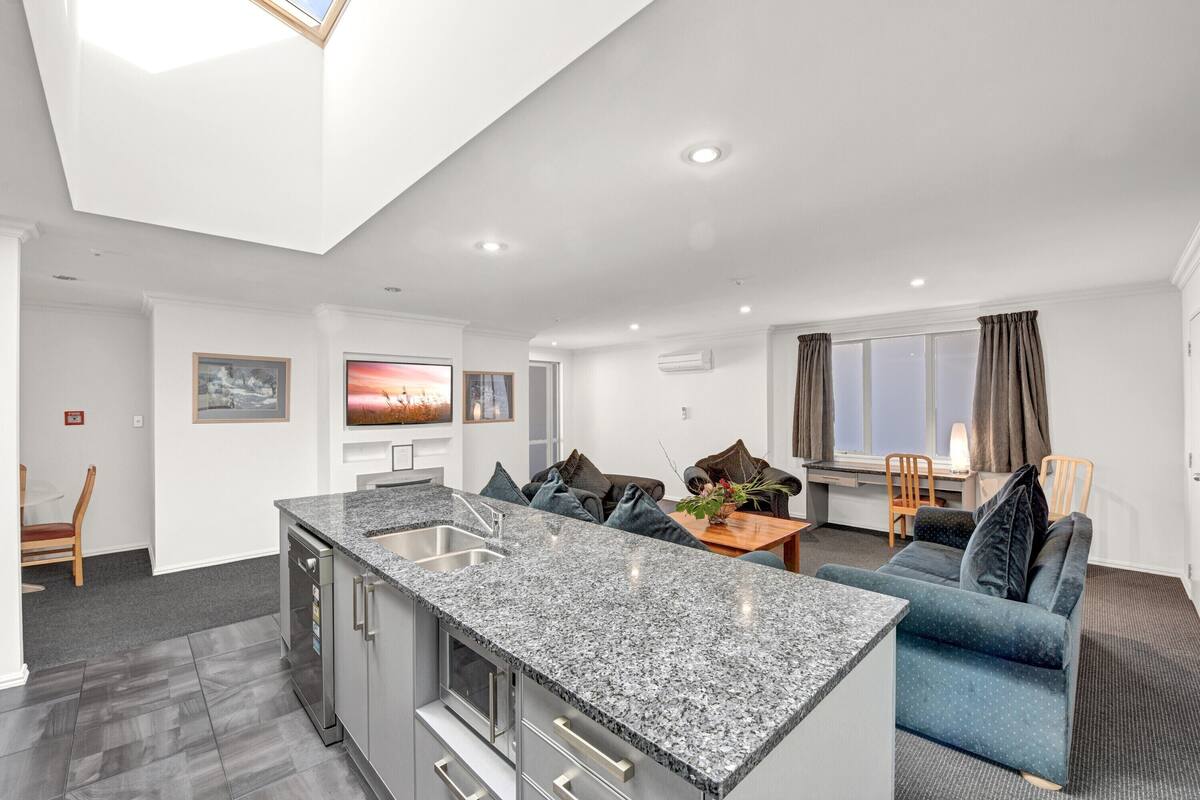 A modern kitchen with granite countertops, a built-in oven, and a dining area with a blue sofa and a small table.
