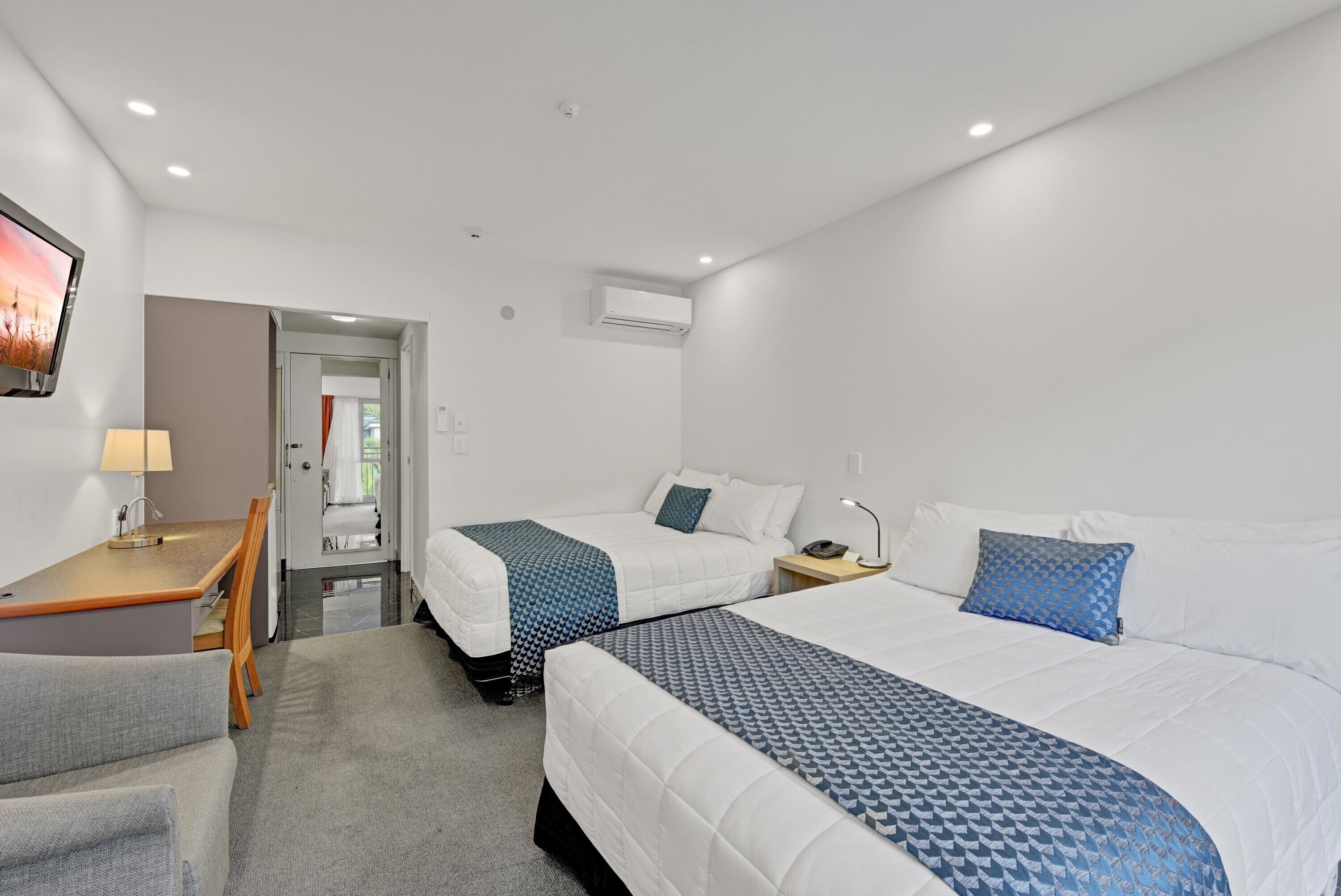 A hotel room with two beds, a desk, a chair, and a TV.