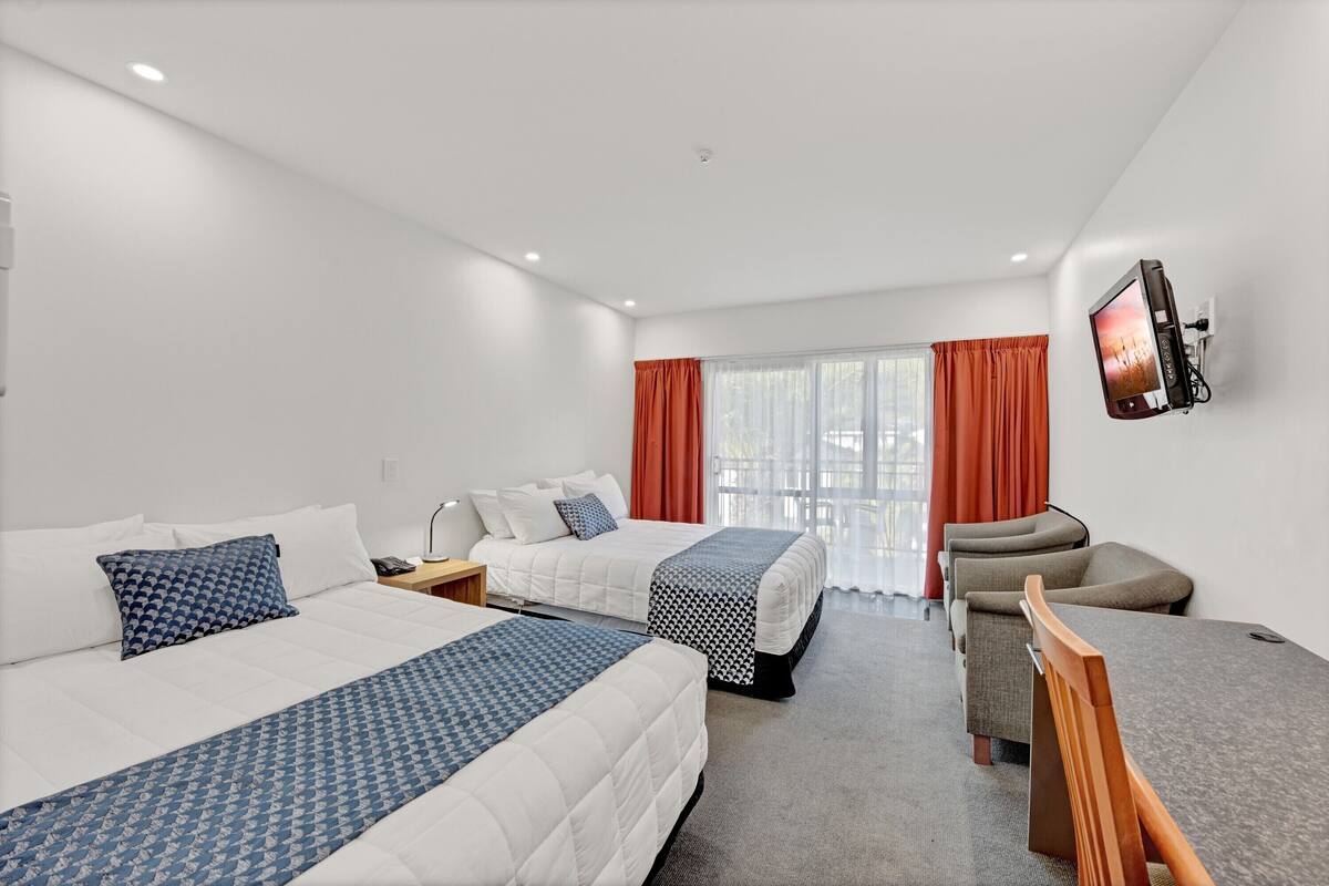 A hotel room with two beds, a TV mounted on the wall, a desk, and a chair.