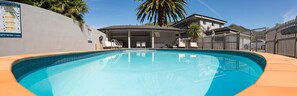 A swimming pool with a covered area, a fence, and a building in the background. - The Hotel Nelson (Nelson)