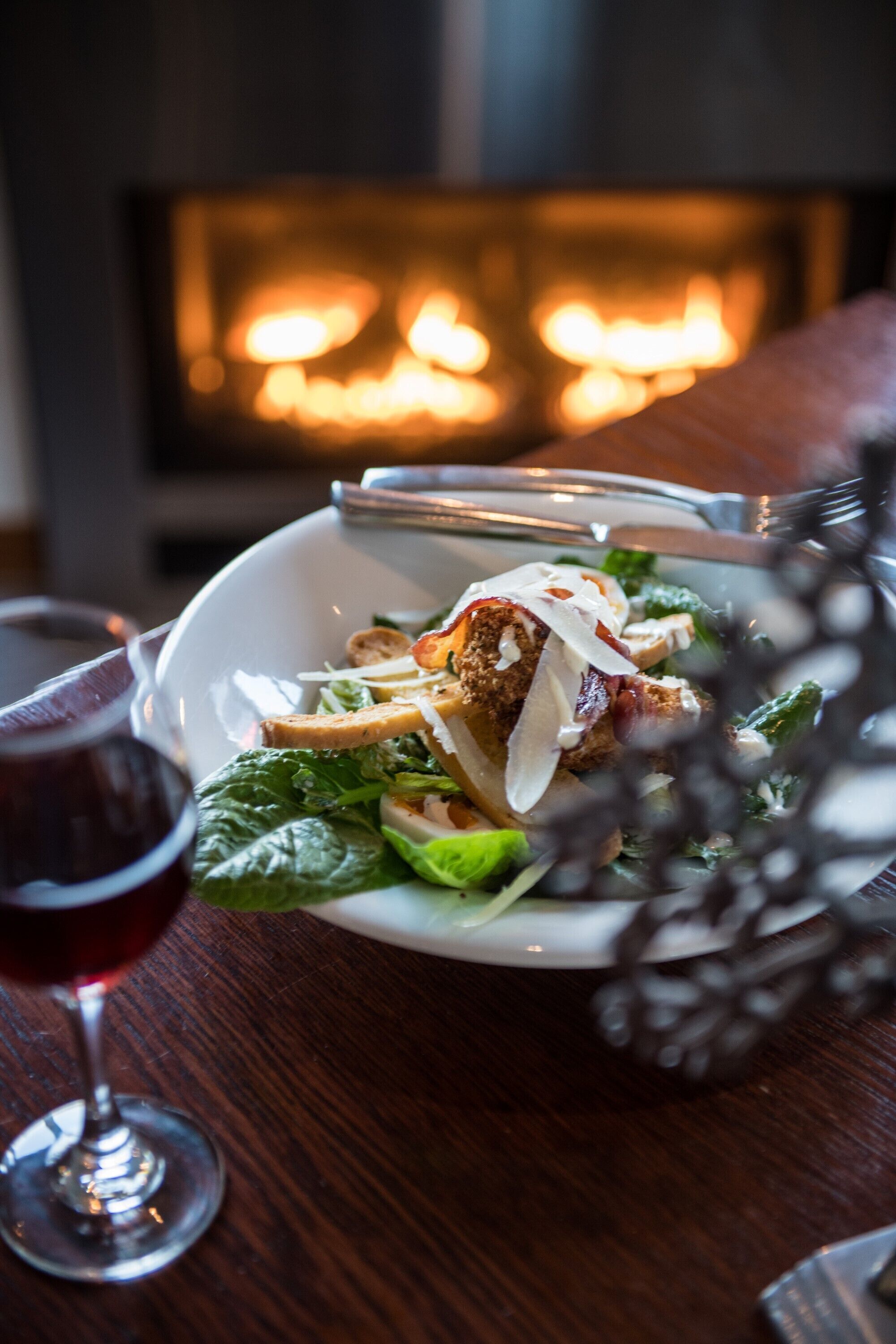 Une assiette de nourriture accompagnée d’un verre de vin rouge, le tout posé sur une table en bois.