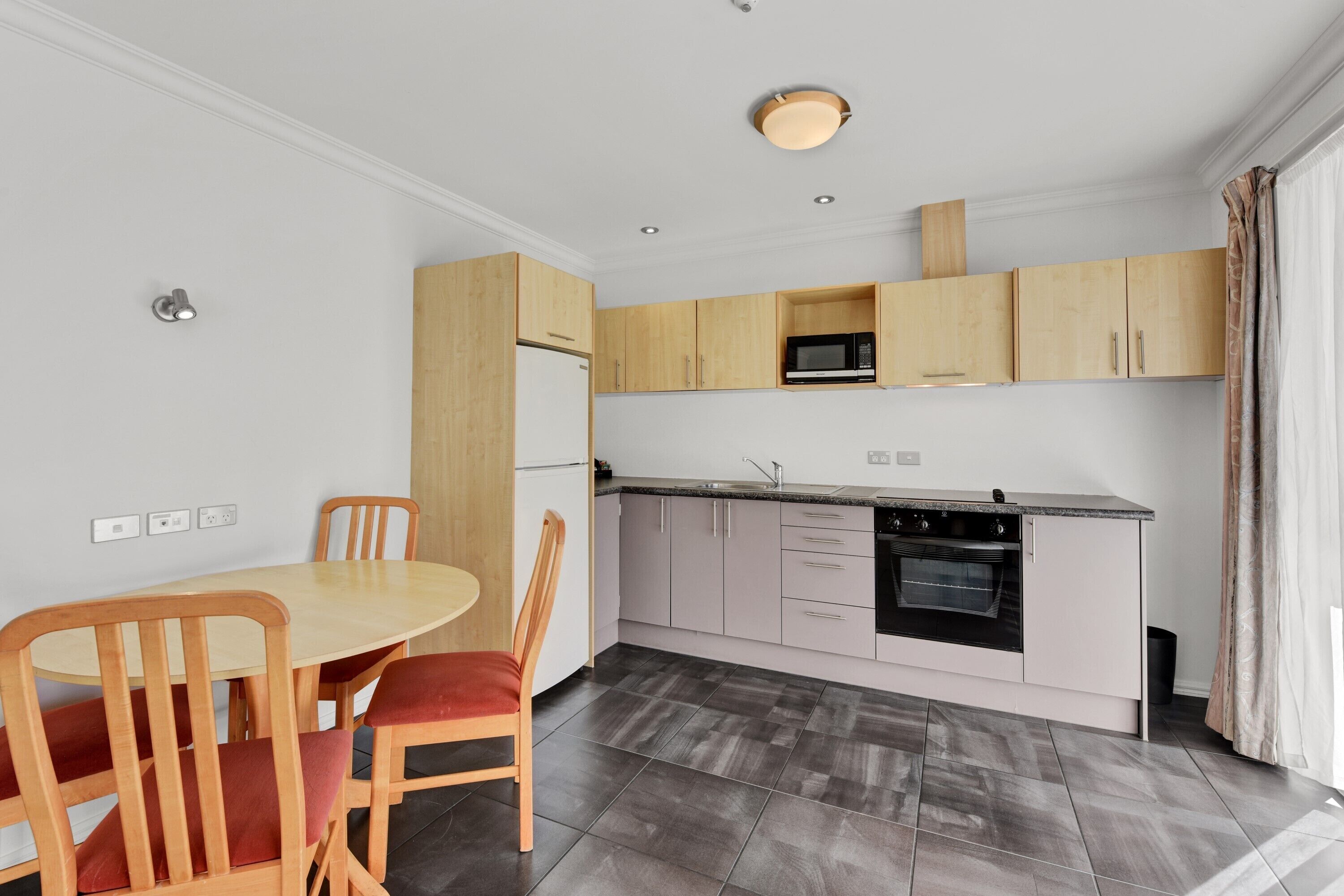 Una cocina moderna con armarios de madera, horno integrado y comedor con mesa y sillas redondas.
