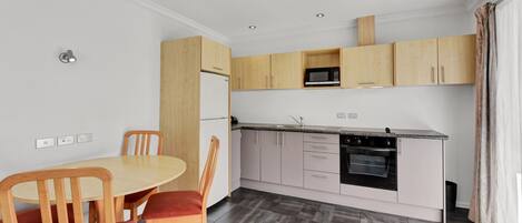 A modern kitchen with wooden cabinets, a built-in oven, and a dining area with a round table and chairs.