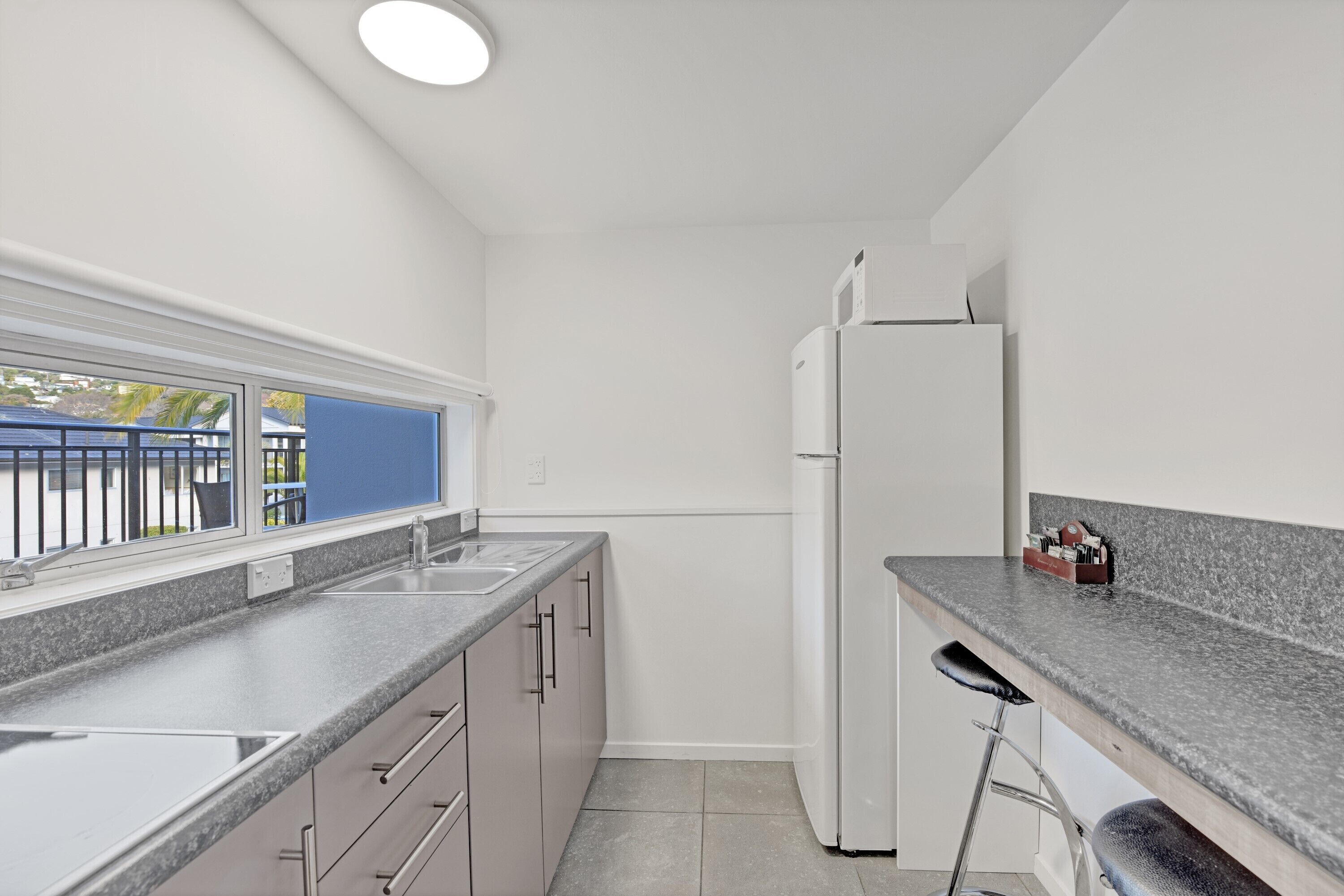 A modern kitchen with a granite countertop, stainless steel appliances, and a window overlooking a blue railing.