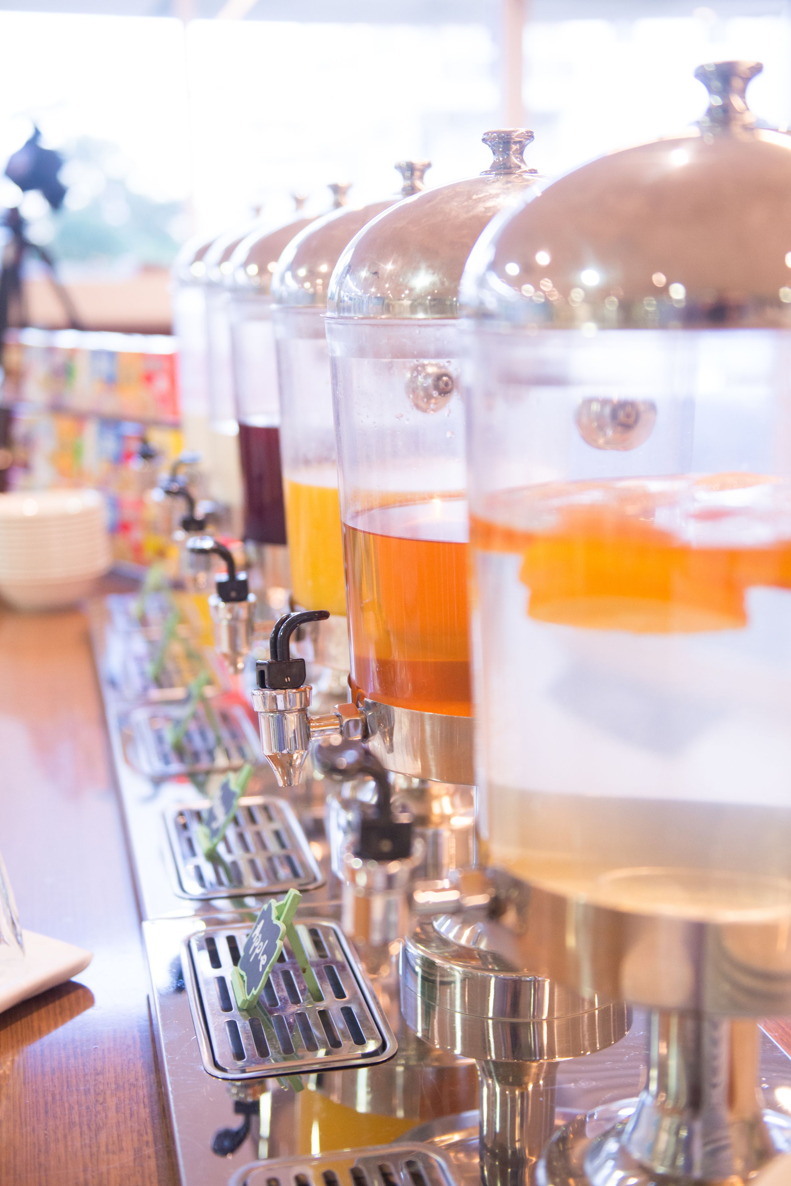 A row of beverage dispensers with clear containers and taps.