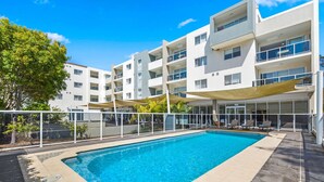 Un hotel moderno con piscina, mobiliario exterior y una zona cubierta con sombrillas.