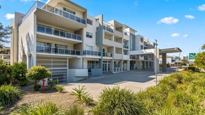 Un hotel moderno de varios pisos con patio central, balcones y una gasolinera al fondo.