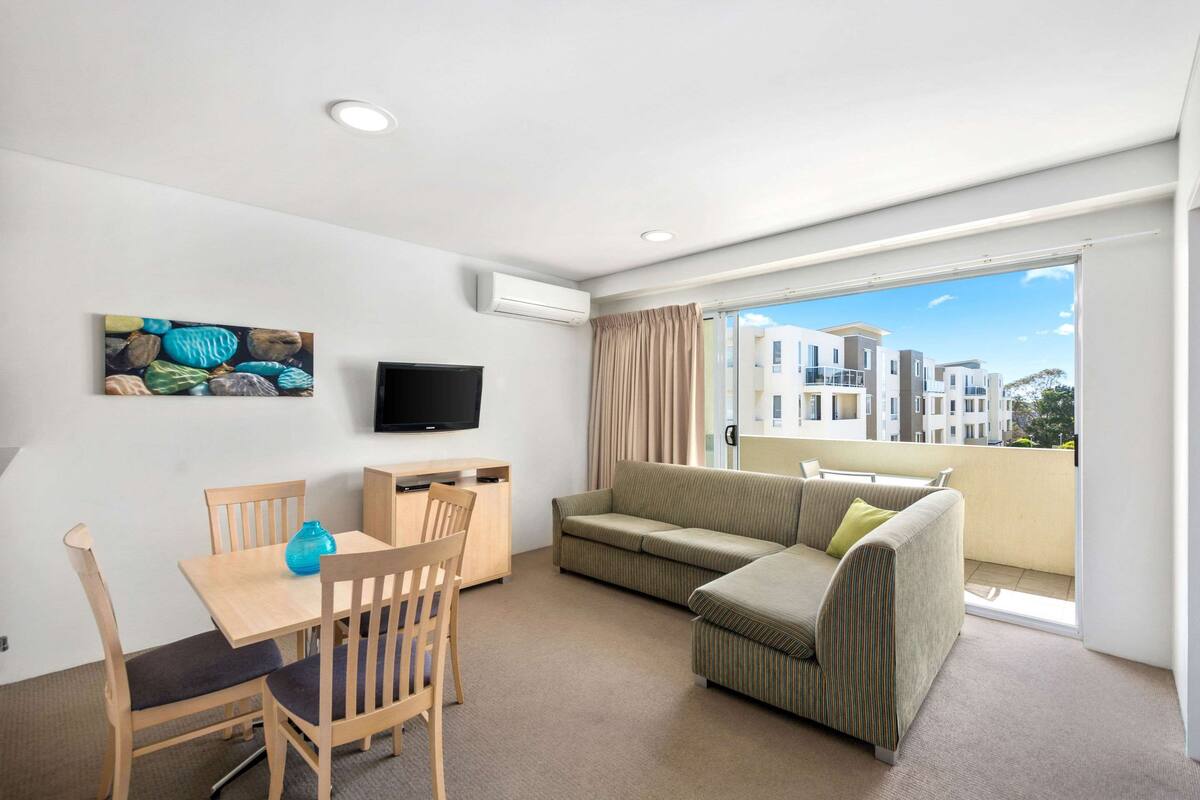 Ein modernes Wohnzimmer mit Essbereich, einem Flachbildfernseher, einer Couch und einem Balkon mit Blick auf die Stadt.