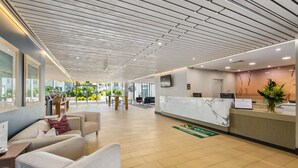 Zona de recepción de hotel con mostrador de mármol, área de descanso con sofás y vistas al exterior.