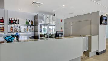 Een moderne hotel receptie met een glazen display vol verschillende drankflessen, een grote airconditioning en een gesloten deur aan de rechterkant.