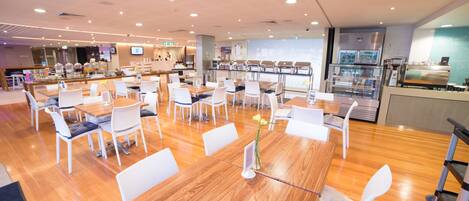 A spacious dining area with wooden tables and white chairs, a buffet counter, and a coffee station.