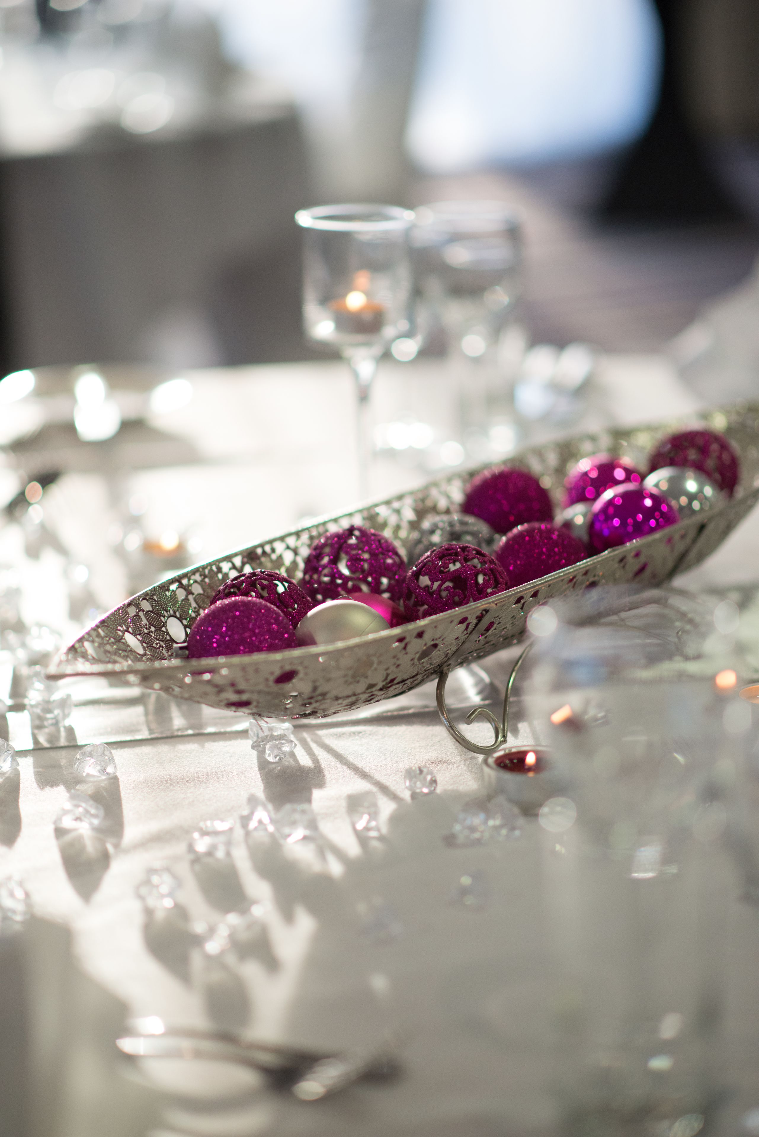 A table with a decorative bowl containing glittery ornaments, clear glassware, and candles.
