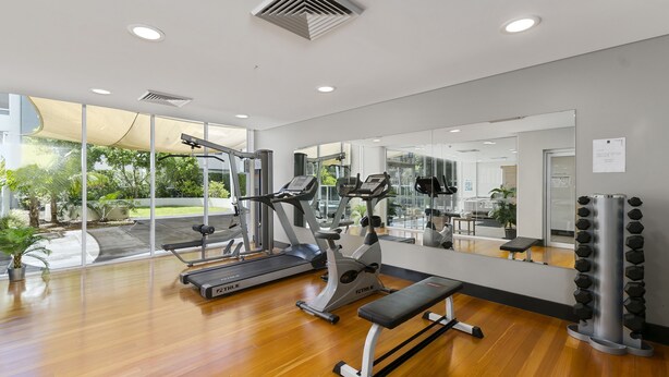 Un gimnasio moderno con equipamiento de ejercicio, amplias ventanas y suelo de madera.