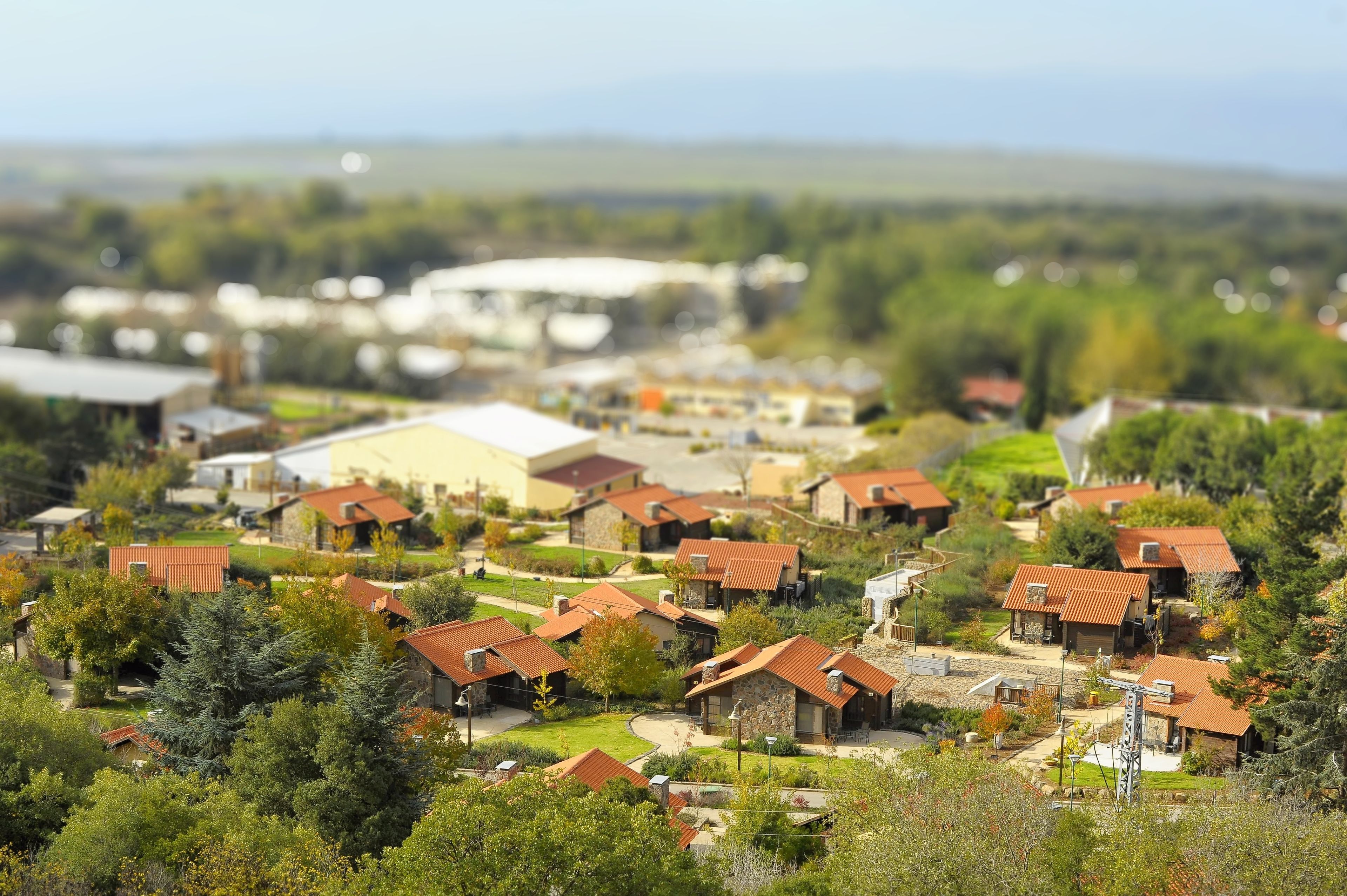A residential area with houses, some with red roofs, surrounded by greenery and a few buildings in the background.