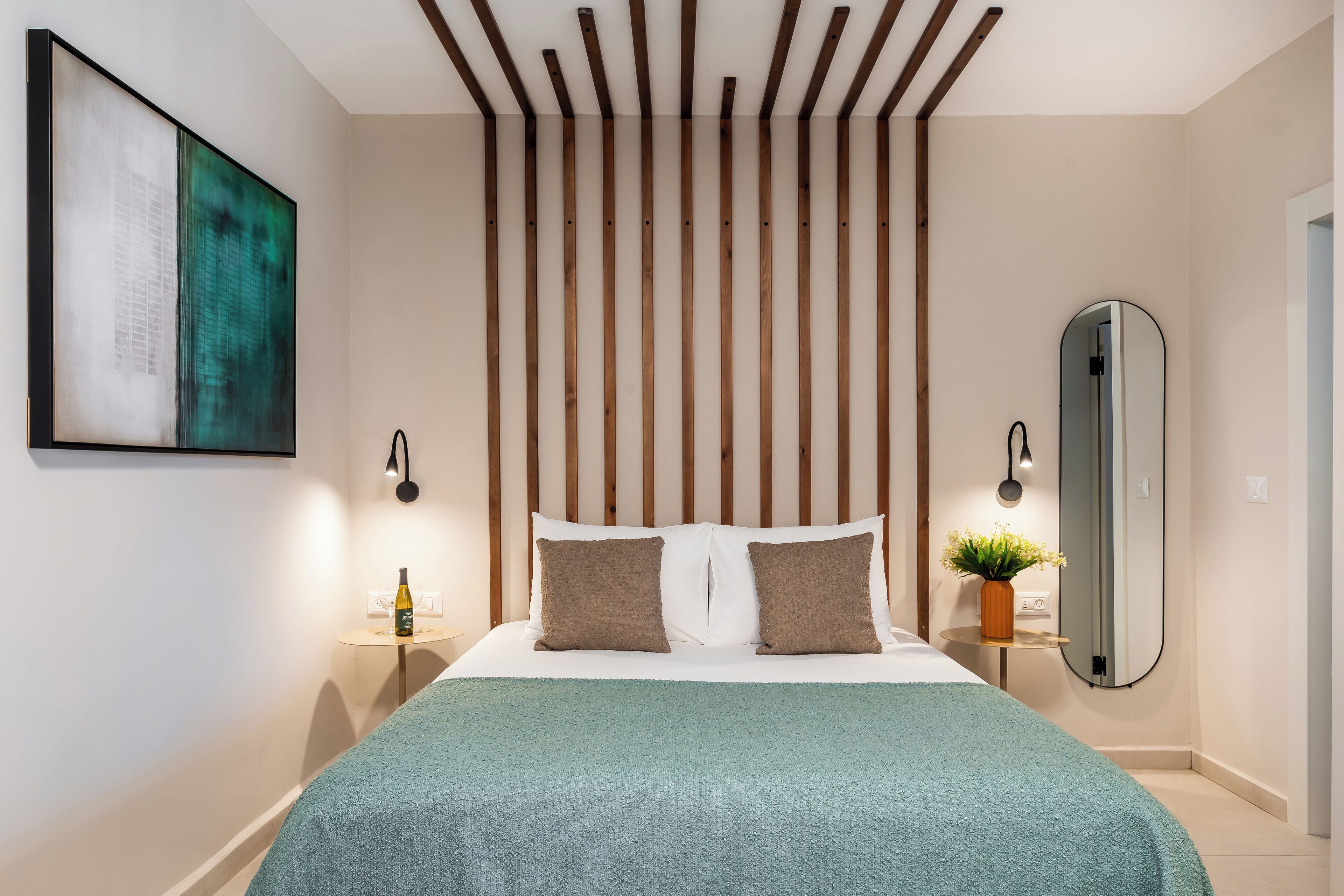 A modern bedroom with a bed, a nightstand, a mirror, and a wall-mounted artwork.