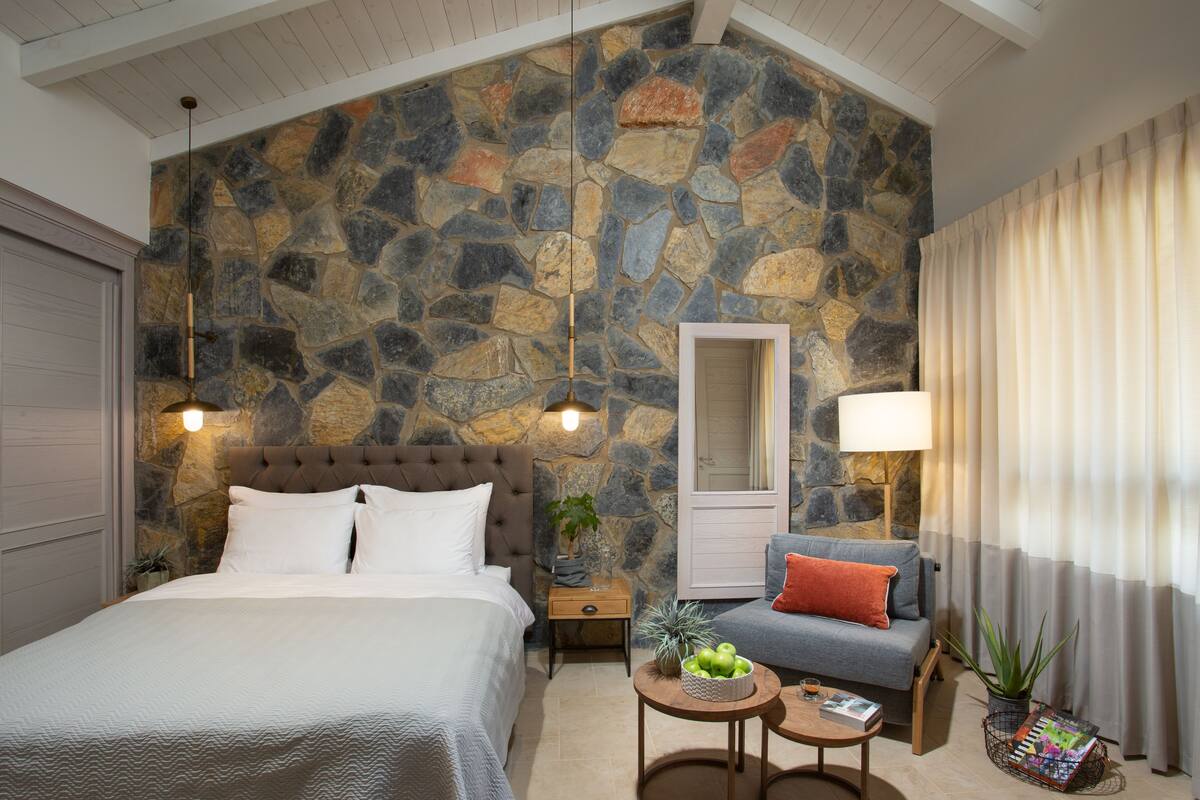 Ein Schlafzimmer mit einer Steinwand, einem Bett, einem Nachttisch, einem Sofa, einem Tisch mit Obstschale und einem Spiegel.