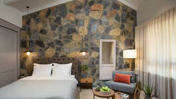 A bedroom with a stone wall, a bed, a nightstand, a sofa, a table with a bowl of fruit, and a mirror.