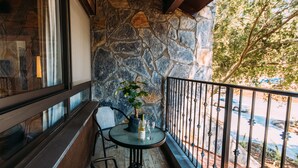 A balcony with stone walls, a table with a bottle and glass, and a chair.