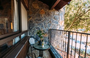 A balcony with stone walls, a table with a bottle and glass, and a chair.