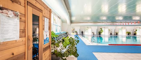 Una piscina interior con colchonetas azules, paredes de madera y plantas en macetas.