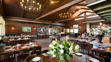 A spacious dining area with wooden tables and chairs, a chandelier, and a large vase of flowers.