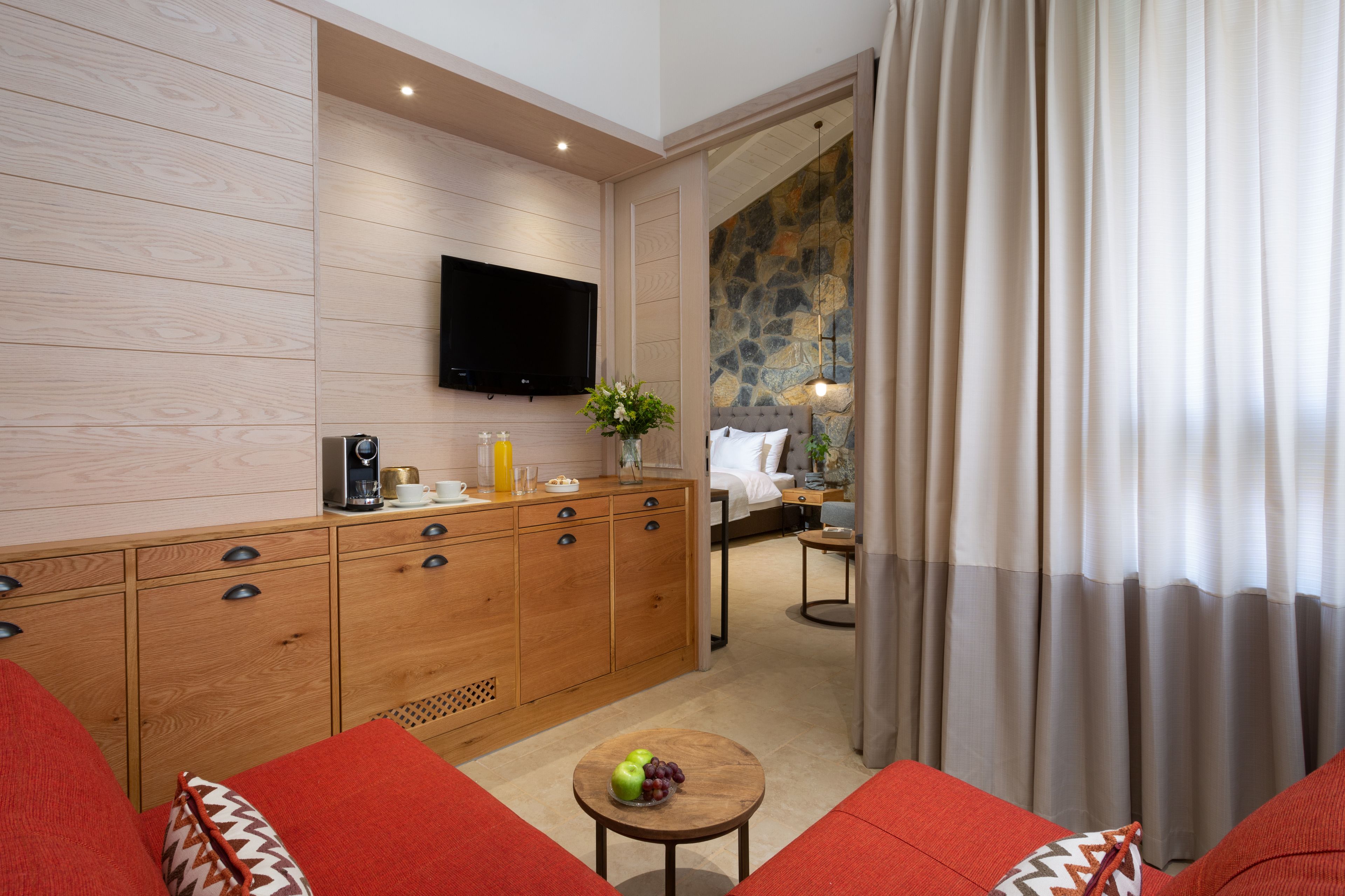 A modern hotel room with a wooden cabinet, a flat-screen TV, a small table with fruit, and a red sofa.