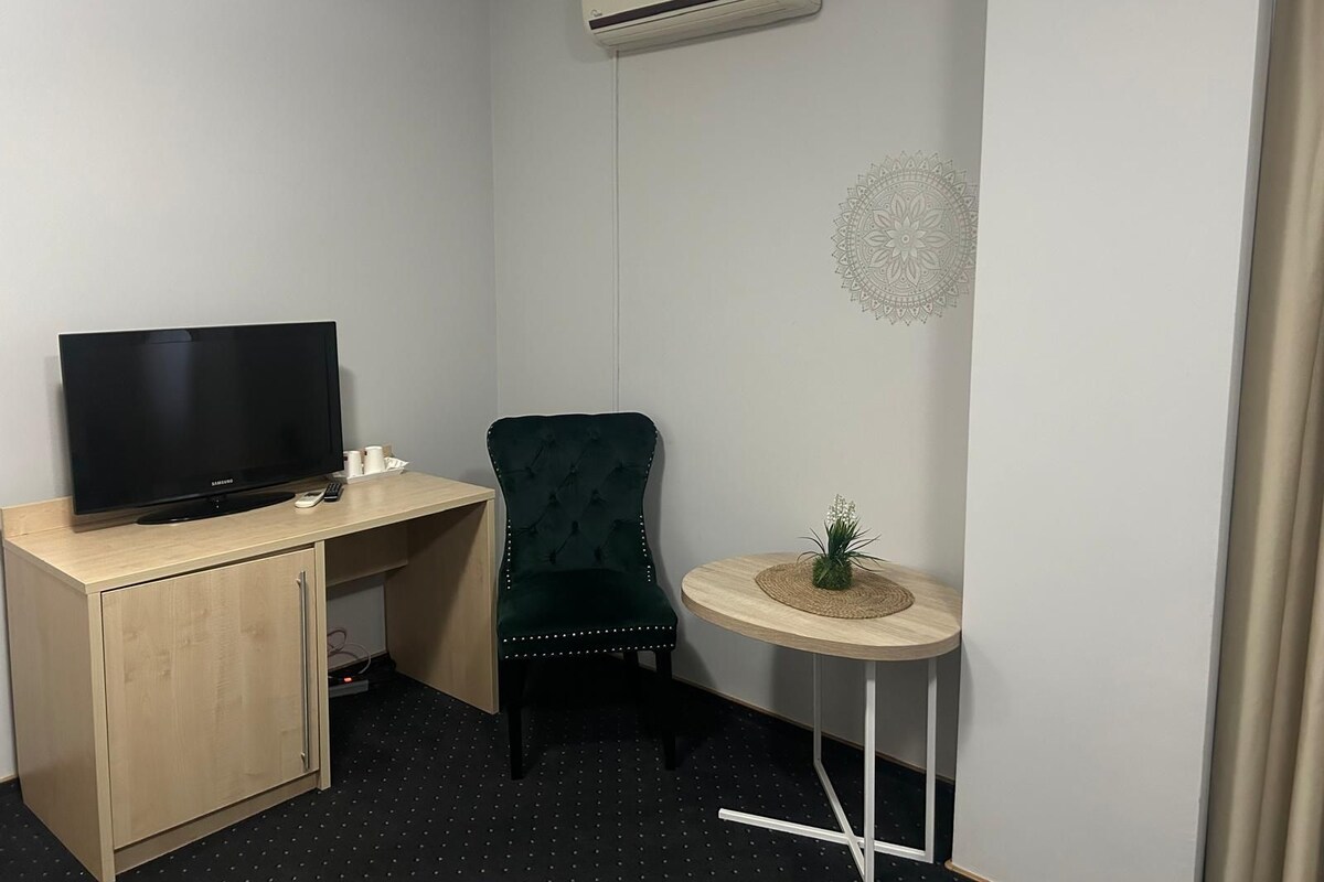 A small office space with a desk, chair, television, and a small table with a plant.