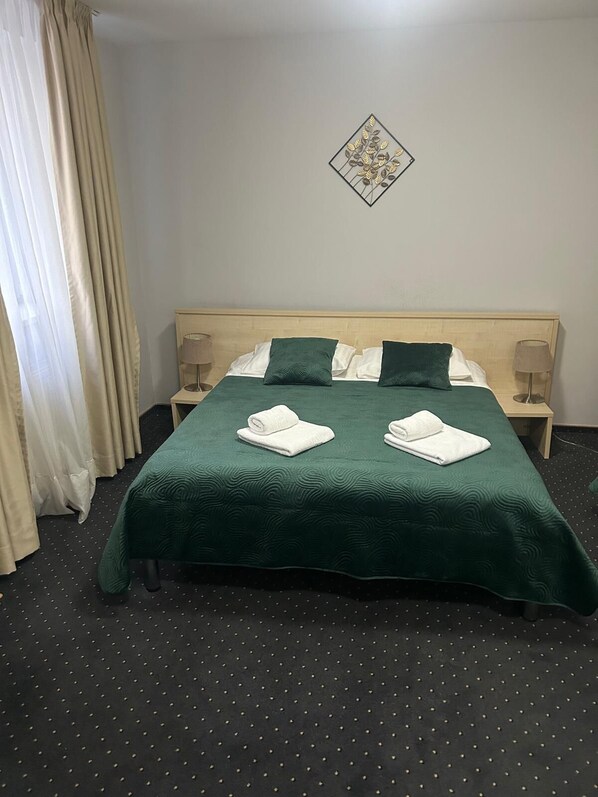 A neatly made bed with green bedding, two pillows, and two rolled towels. There is a wall decoration above the bed and a lamp on each side. - Hotel Pacific Timisoara (Timisoara)