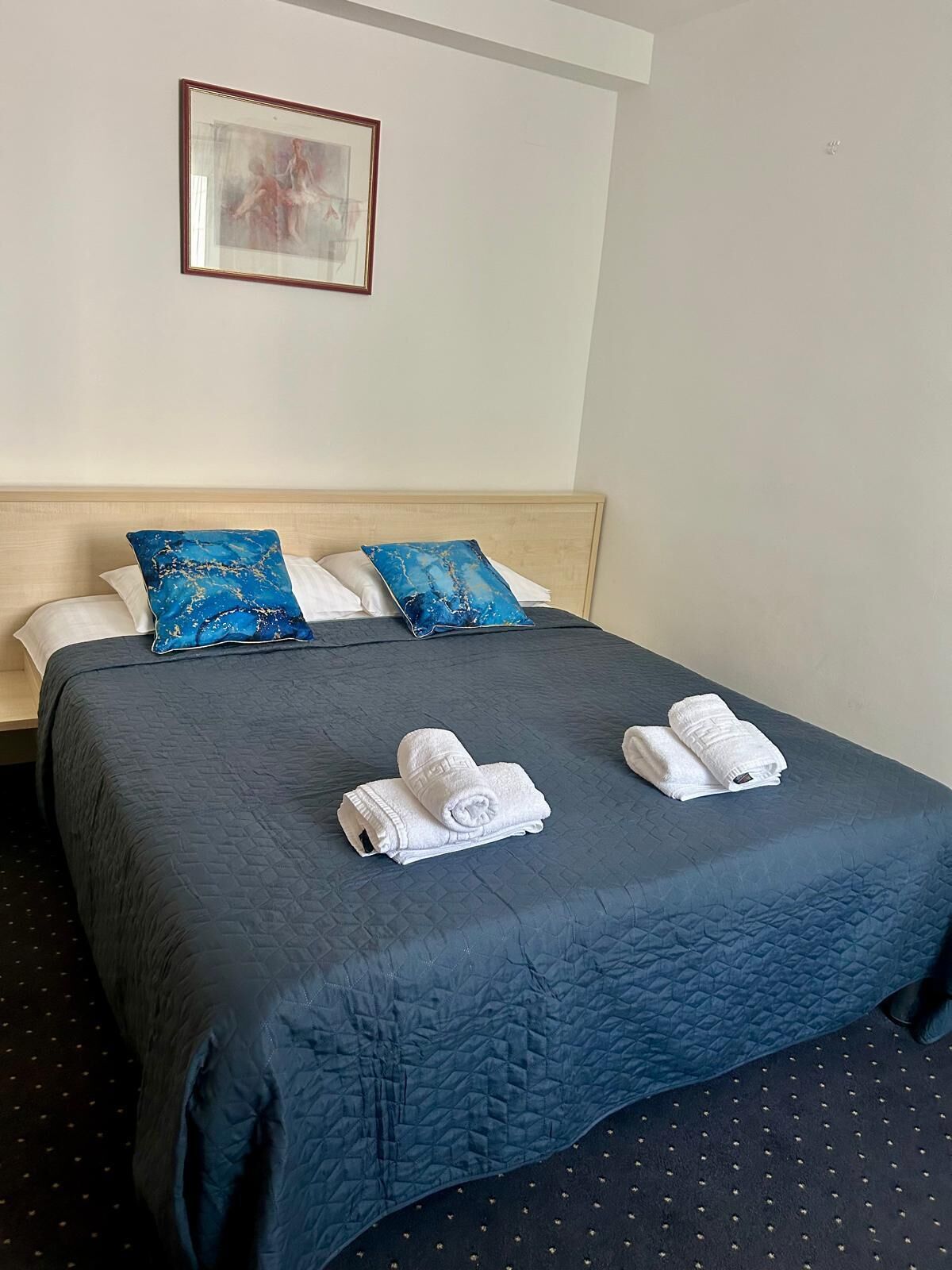 Ein Hotelzimmer mit einem dunkelblauen, gesteppten Bettüberwurf, zwei weißen Handtüchern und zwei blauen Kissen.