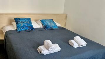 Ein Hotelzimmer mit einem dunkelblauen, gesteppten Bettüberwurf, zwei weißen Handtüchern und zwei blauen Kissen.