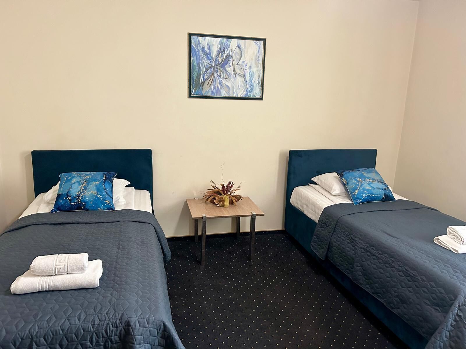 Quarto de hotel com duas camas, uma mesa pequena e uma obra de arte emoldurada na parede.