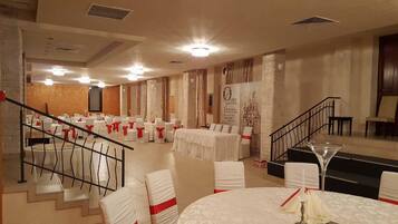 Un salón de banquetes con mesas redondas, sillas blancas con cintas rojas y una escalera.