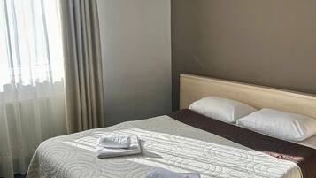 A neatly made bed with a beige quilt, two rolled towels, and a brown throw blanket.