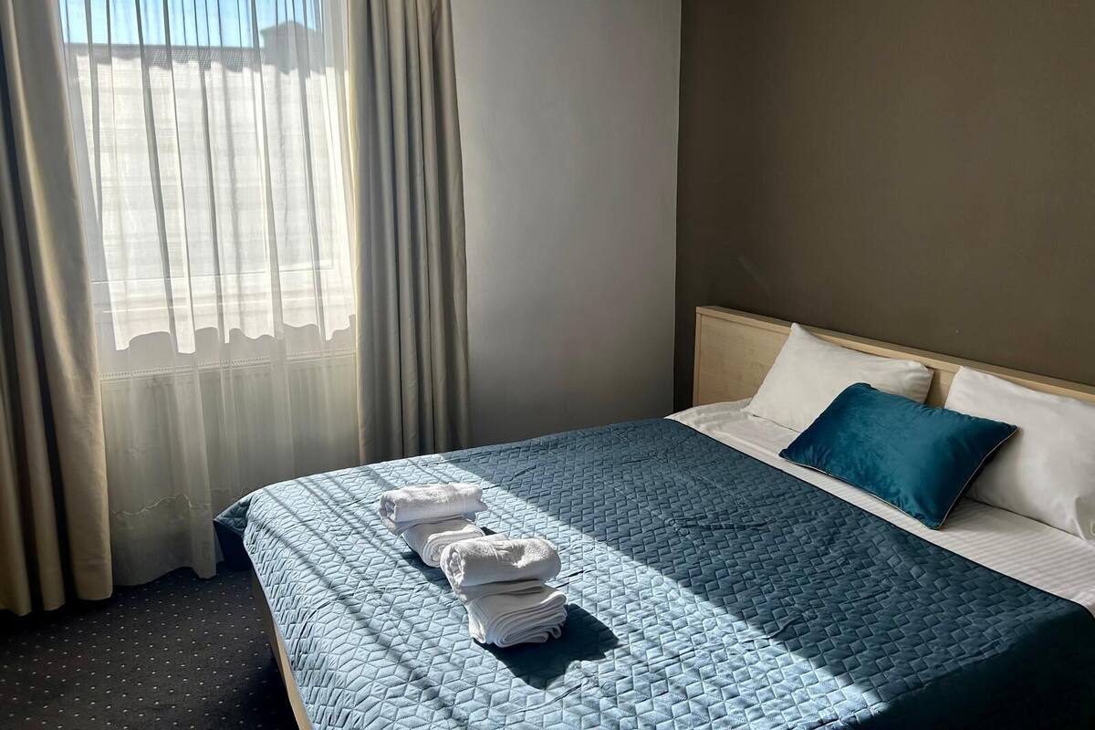 A hotel room with a bed, a window with curtains, and a neatly folded towel on the bed.
