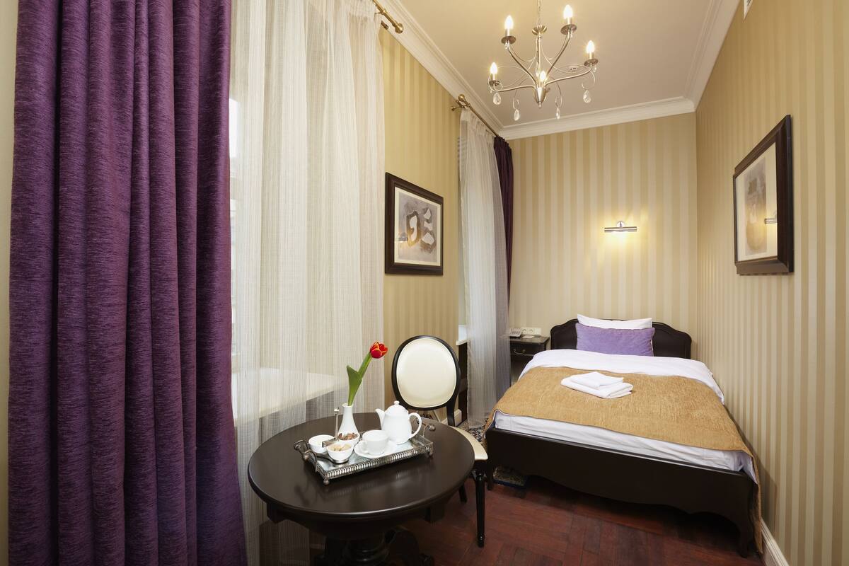 Une chambre d'hôtel avec un lit, une table de chevet sur laquelle se trouve un plateau de petit-déjeuner, une chaise et un lustre.