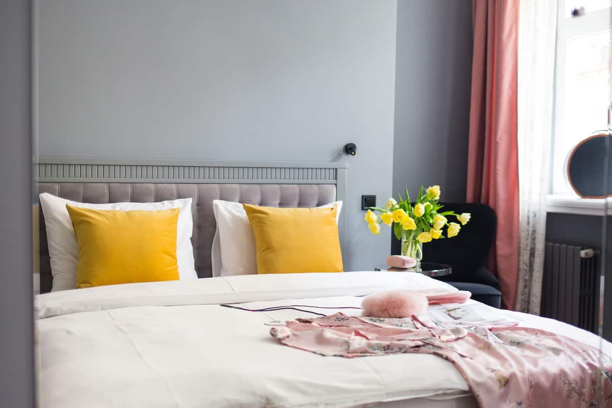Un lit bien fait, recouvert d’une courtepointe à motifs floraux blancs et roses, avec deux oreillers jaunes et blancs, et un vase rempli de fleurs jaunes posé sur une table de chevet.