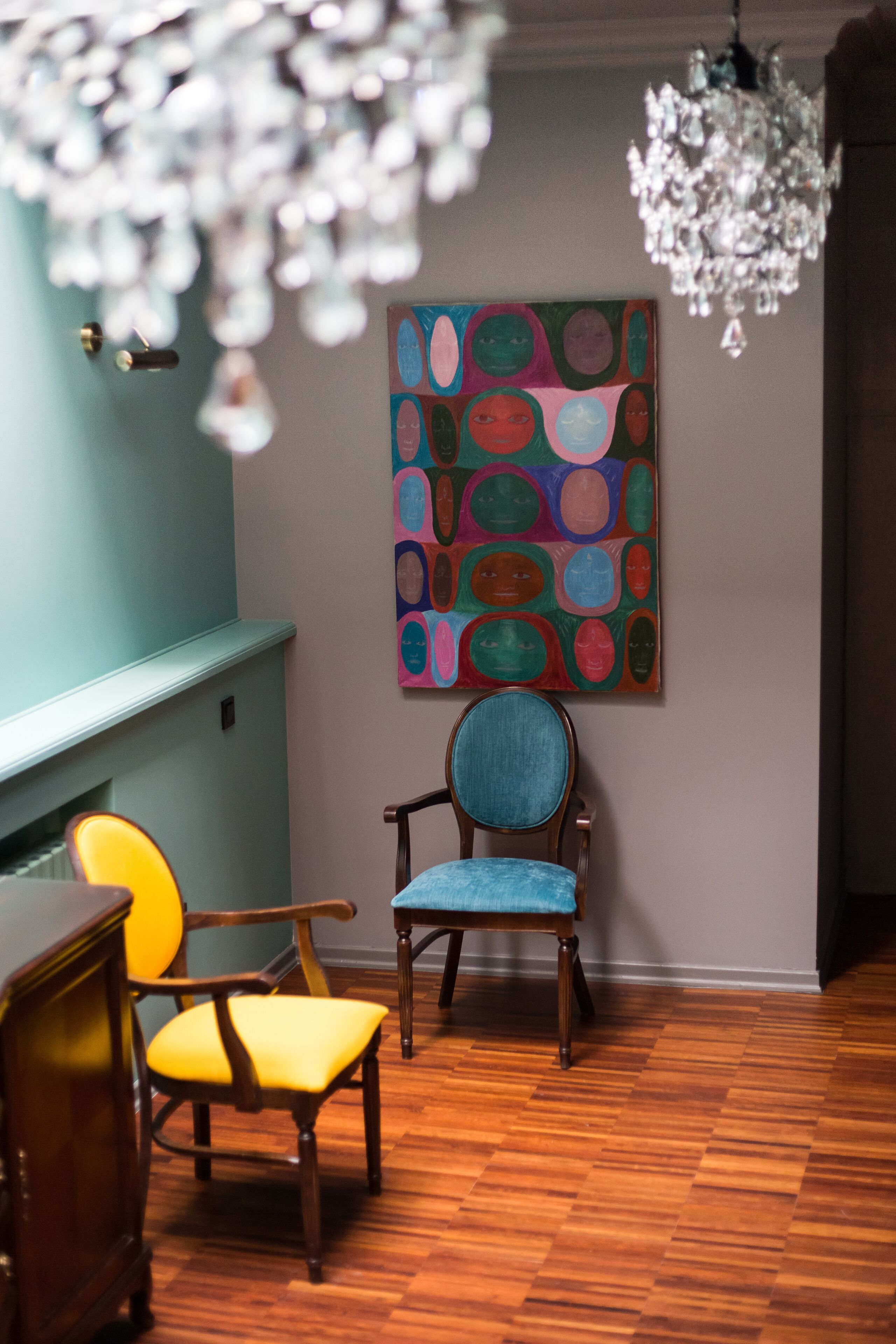 Una habitació amb sòl de fusta, paret blava, un quadre abstracte i ple de colors, i un penjador.