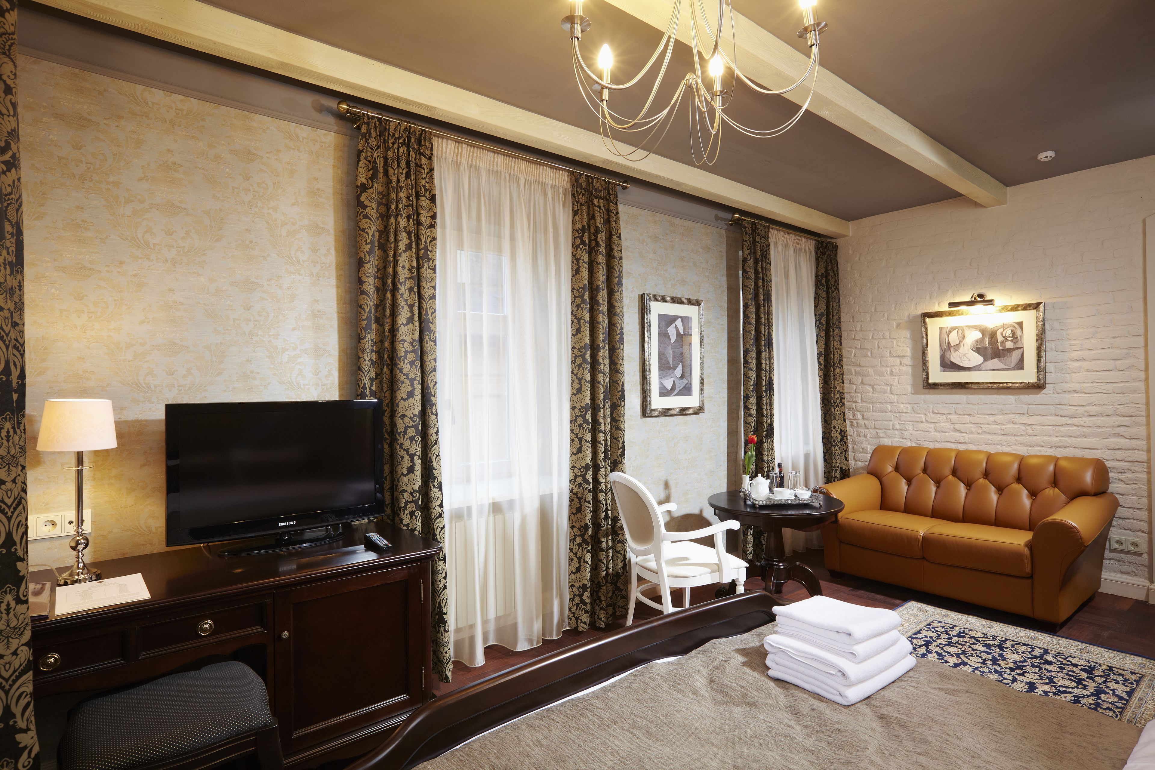 Une chambre d’hôtel équipée d’une télévision, d’un canapé, d’un bureau avec une lampe, d’une chaise et d’un lit avec une serviette blanche pliée.