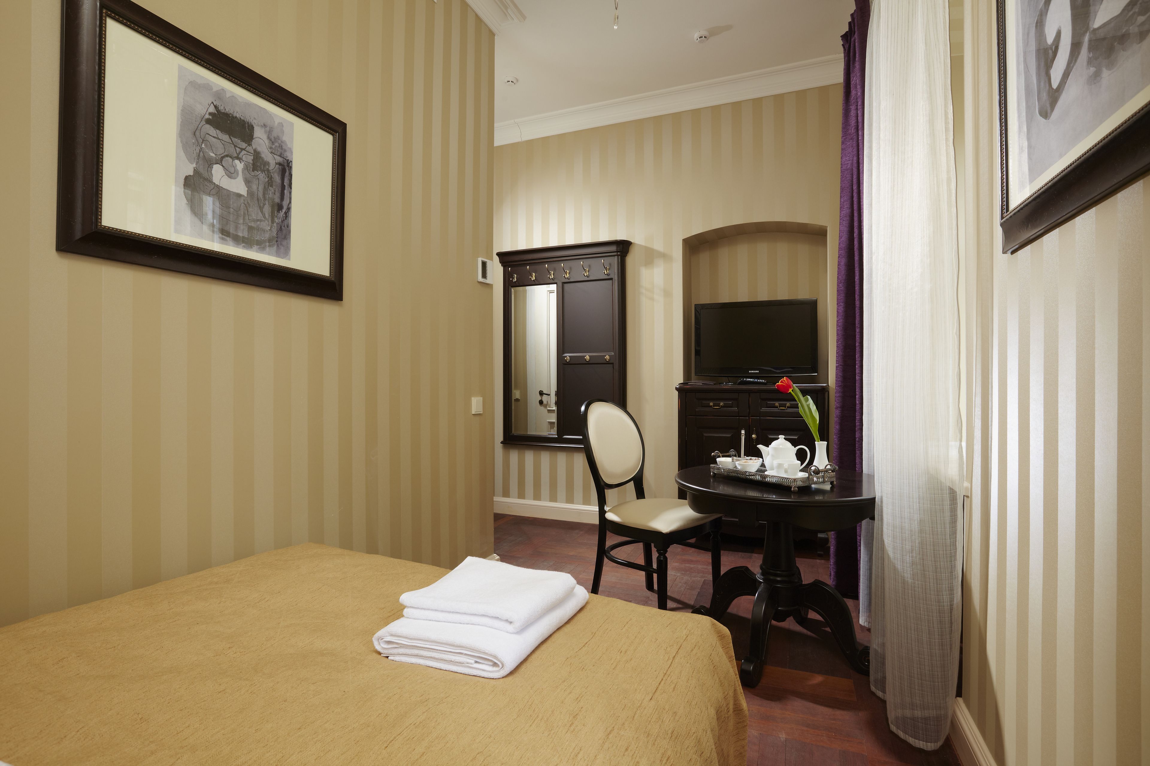A hotel room with a bed, a desk with a chair, a television, and a mirror.