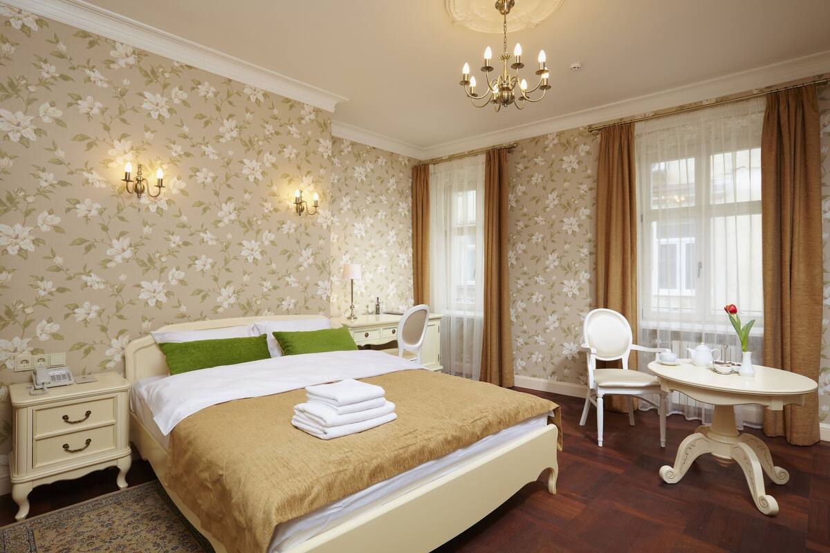 Une chambre d’hôtel comprenant un lit, une table de chevet, une lampe, une chaise et une petite table sur laquelle se trouve un vase.
