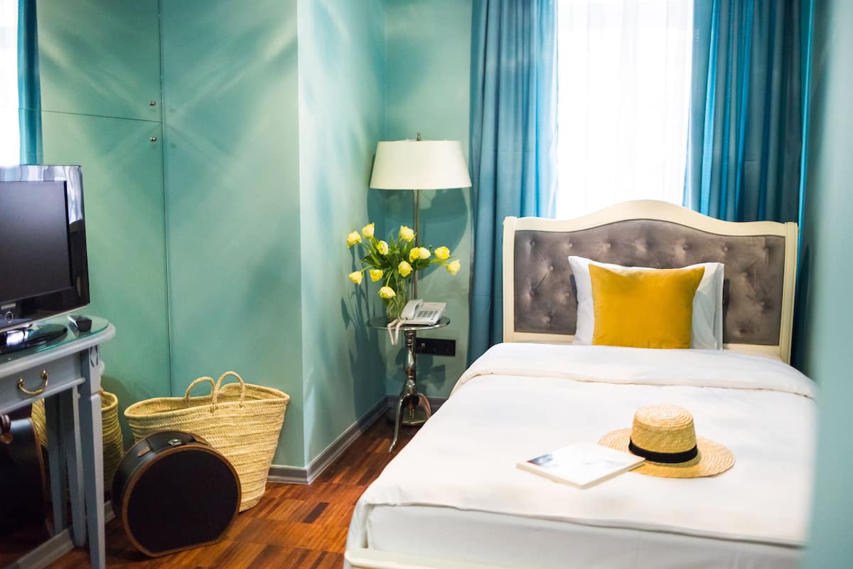 Une chambre d’hôtel avec un lit, une télévision, une lampe, un vase avec des fleurs et une valise.