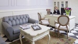 A hotel lobby with a grey sofa, a white reception desk, and a chandelier.