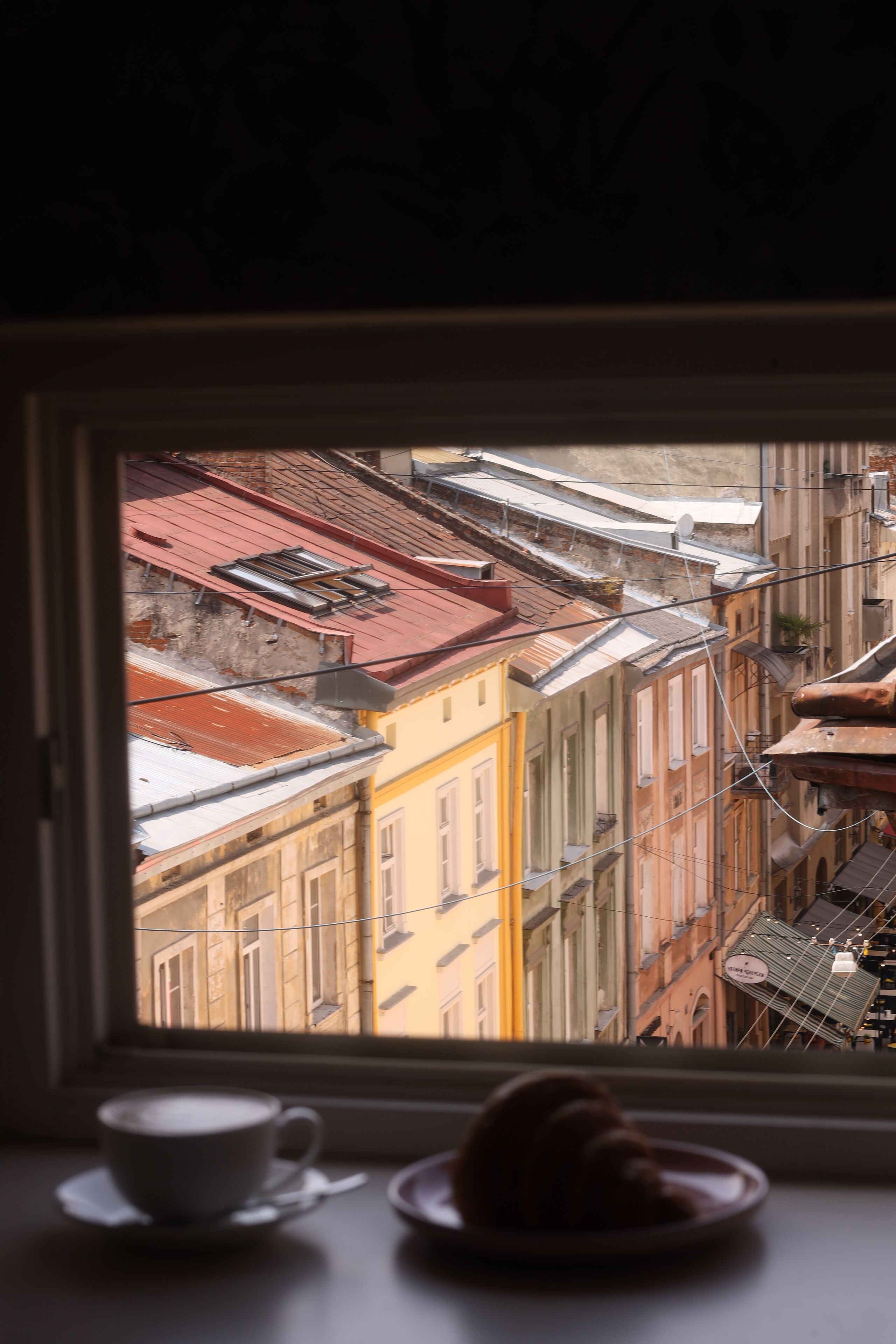 A window view of a cityscape with buildings and a cup of coffee on a table.