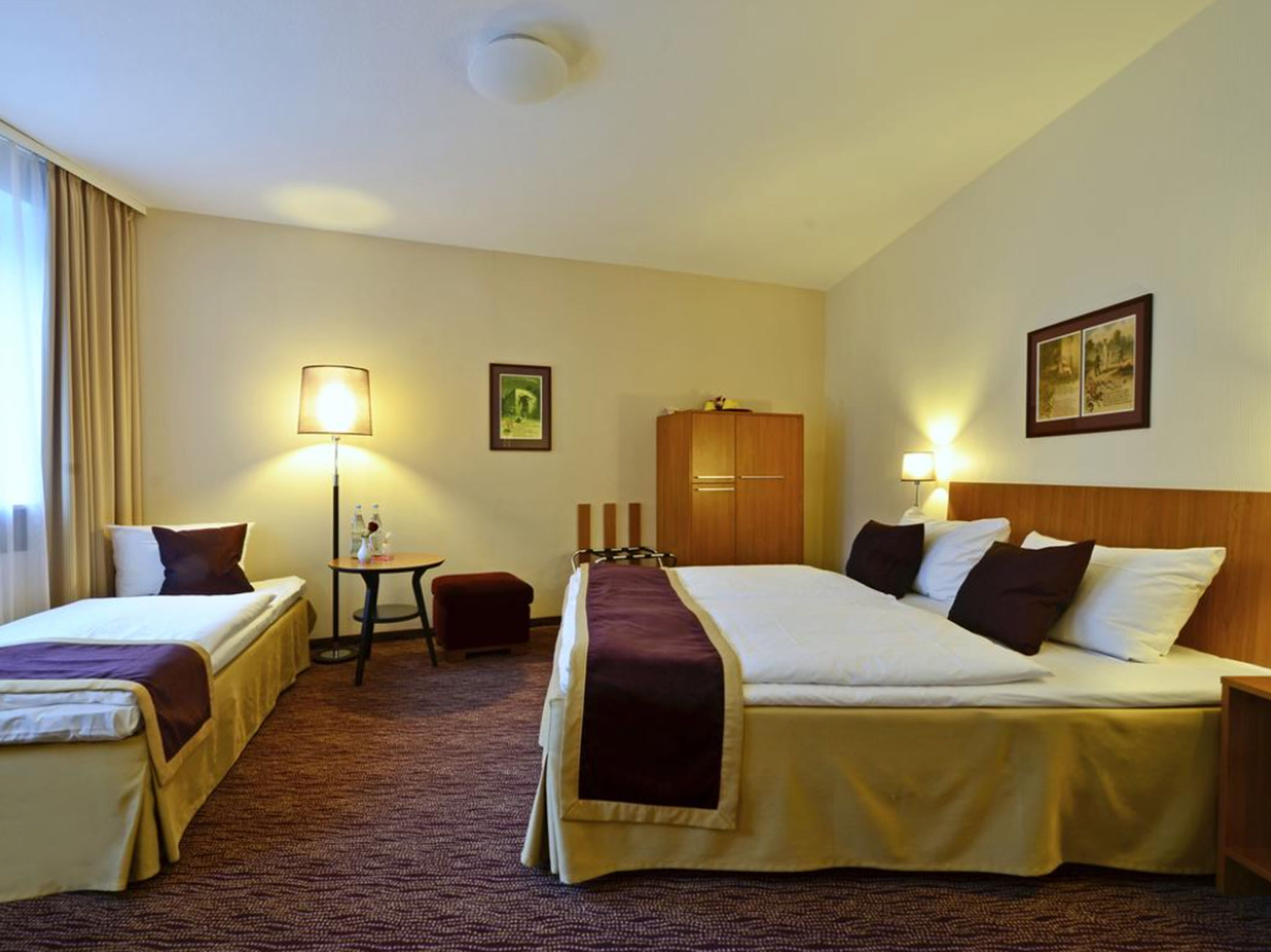 Habitación de hotel con dos camas, un escritorio, una silla, un armario y una lámpara.