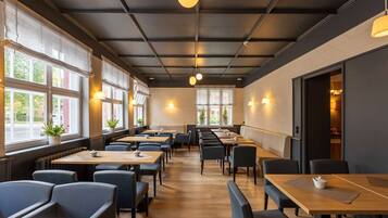 A modern restaurant with long tables and booths, large windows with blinds, and pendant lighting.
